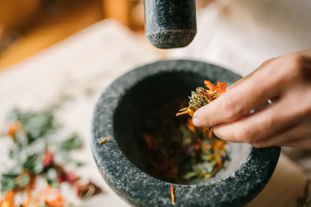 A heavy stone mortar and pestle being used to grind toasted spices